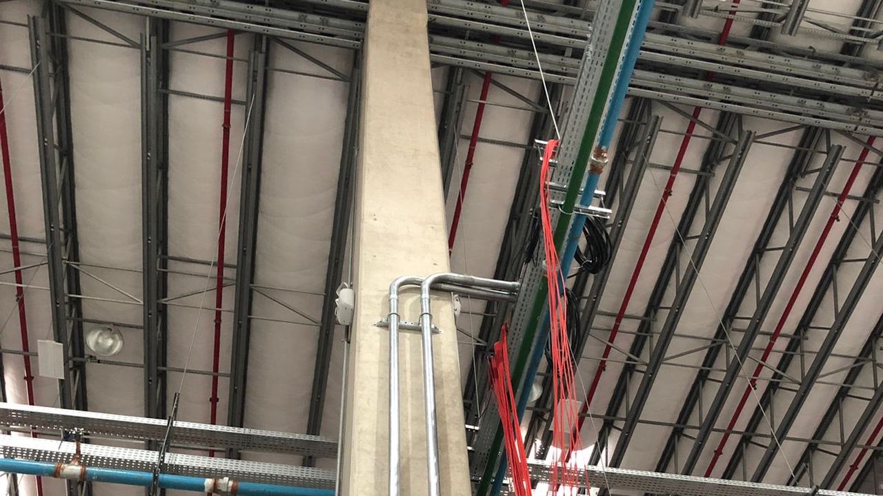Caixa de passagem IP66 instalada em coluna estrutural, no teto de galpão logístico, com eletrocalhas e cabos de fibra