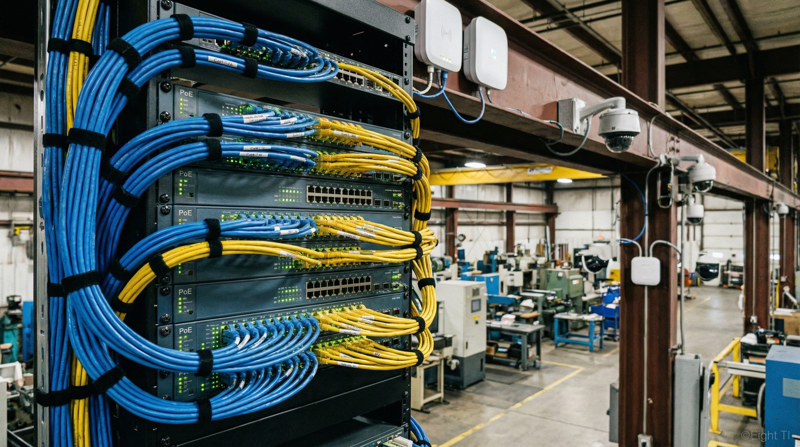 Rack de rede industrial com switches PoE, câmeras IP e access points em fábrica - Eight TI