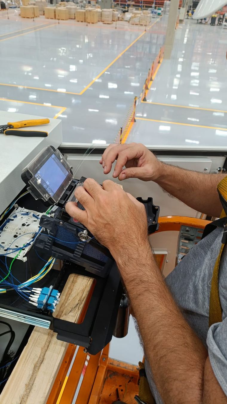 Técnico operando máquina de fusão de fibra óptica para emenda de backbone, com conectores LC organizados